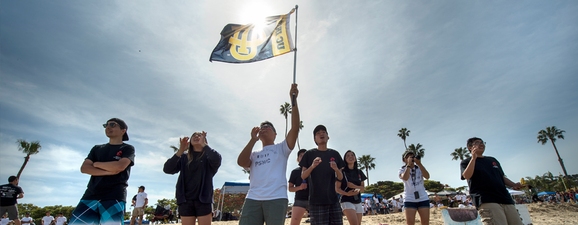 Group of UCI alumni holding up school flag