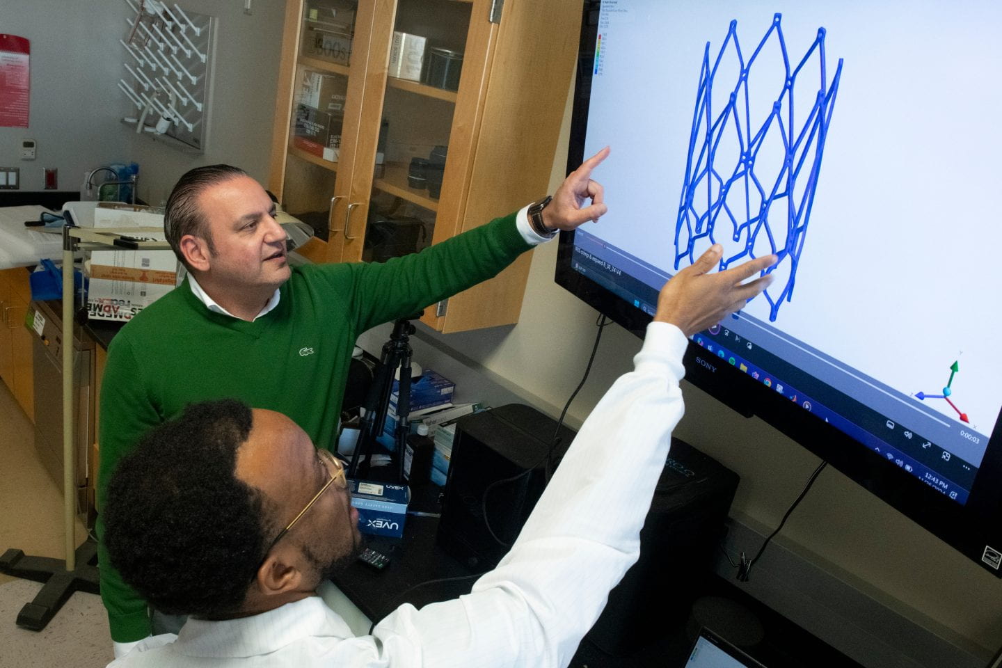 Nnaoma Agwu (pointing), a Ph.D. candidate in biomedical engineering at UC Irvine, and his advisor, professor Arash Kheradvar, examine an image illustrating the transcatheter implantation of the Iris Valve. Steve Zylius / UC Irvine