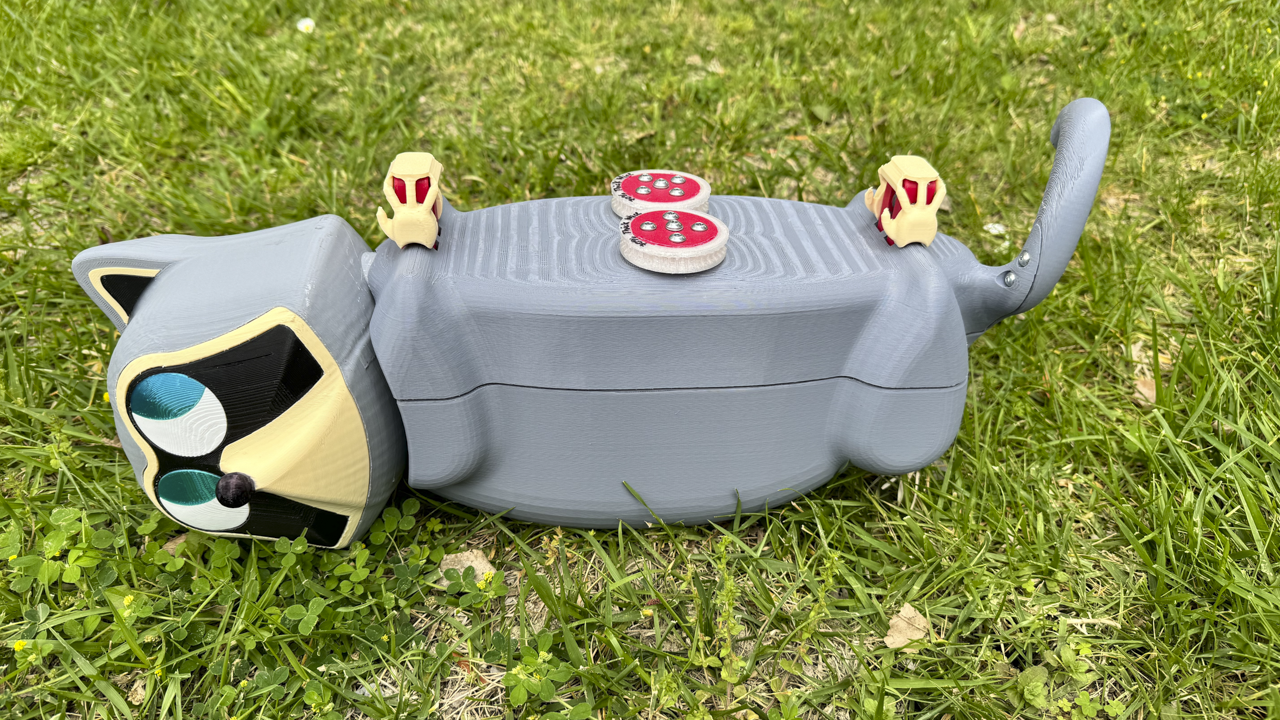 Grey robot cat lying in grass.